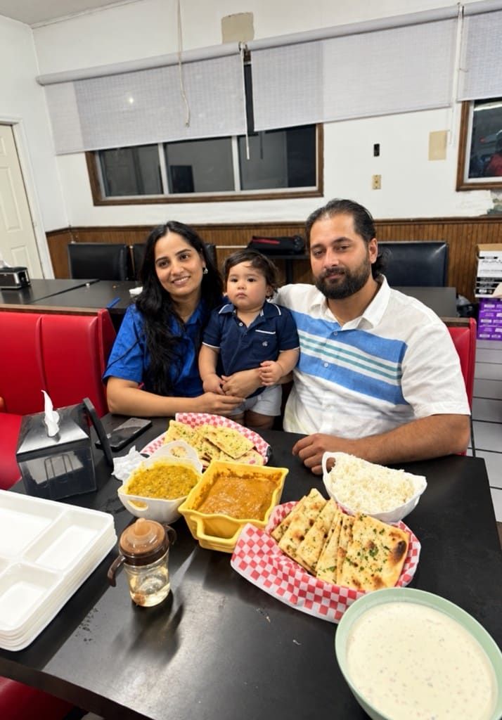 A family with a toddler at a booth, with dal, curry, rice, naan, and raita on the table